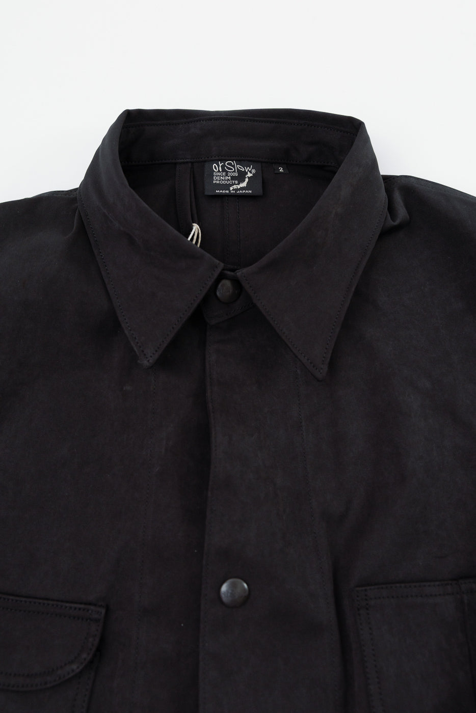 Close-up front view of the collar and upper buttons of a black OrSlow shirt.