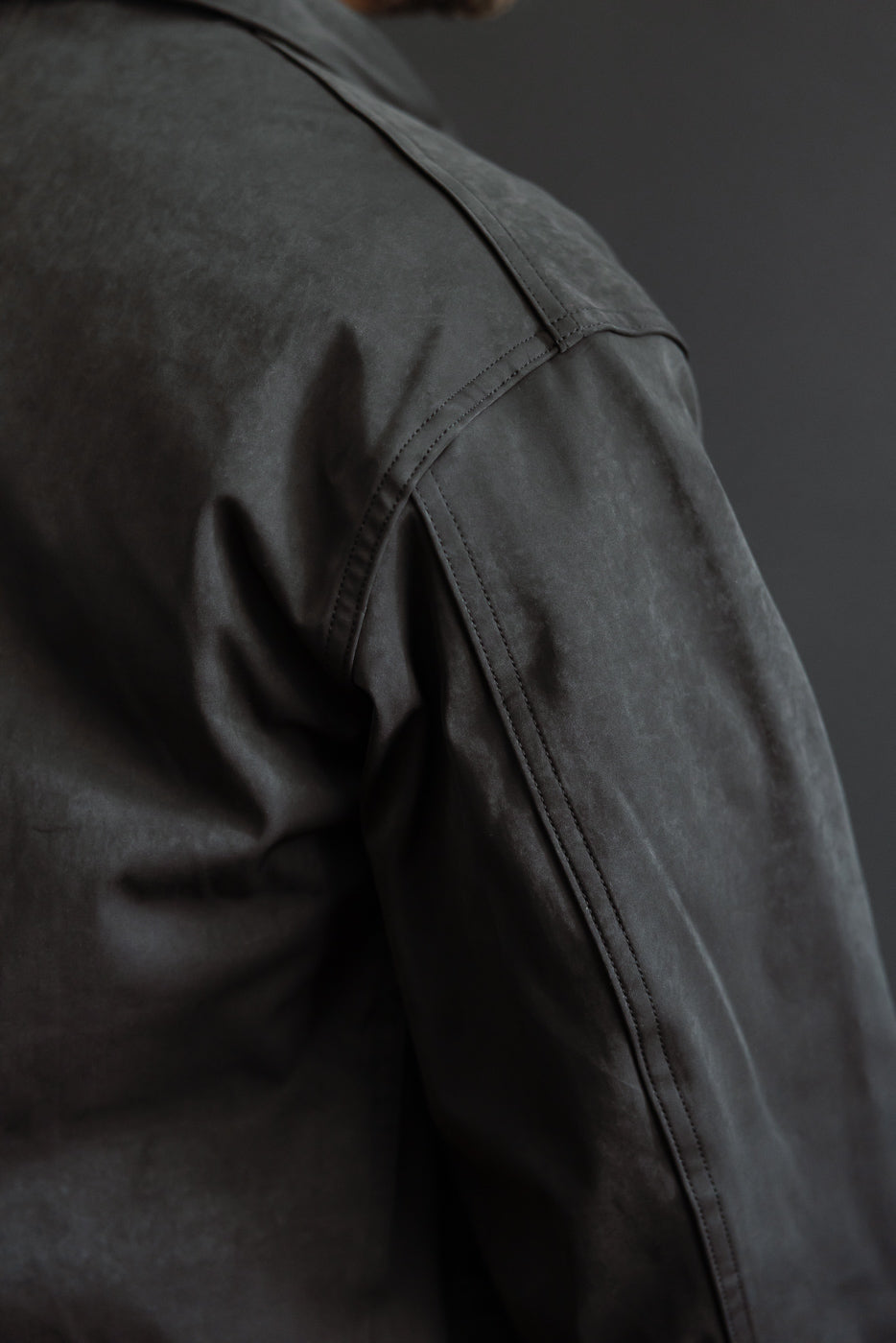 Close-up of the back right shoulder and sleeve of a grey jacket on a male model, 5'9