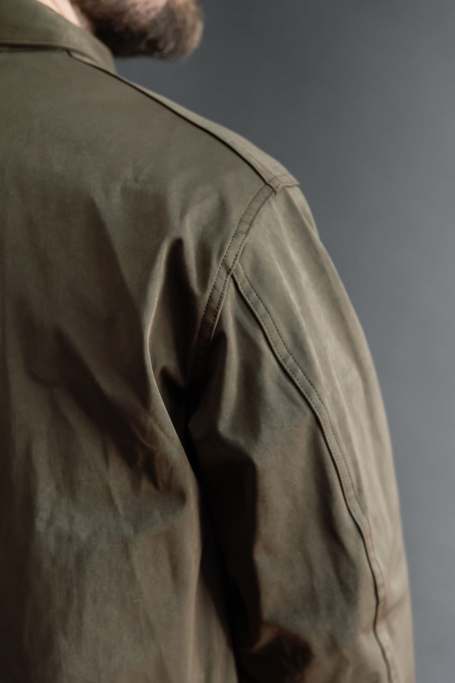 Close-up of the back and shoulder of an olive green canvas jacket on a male model.