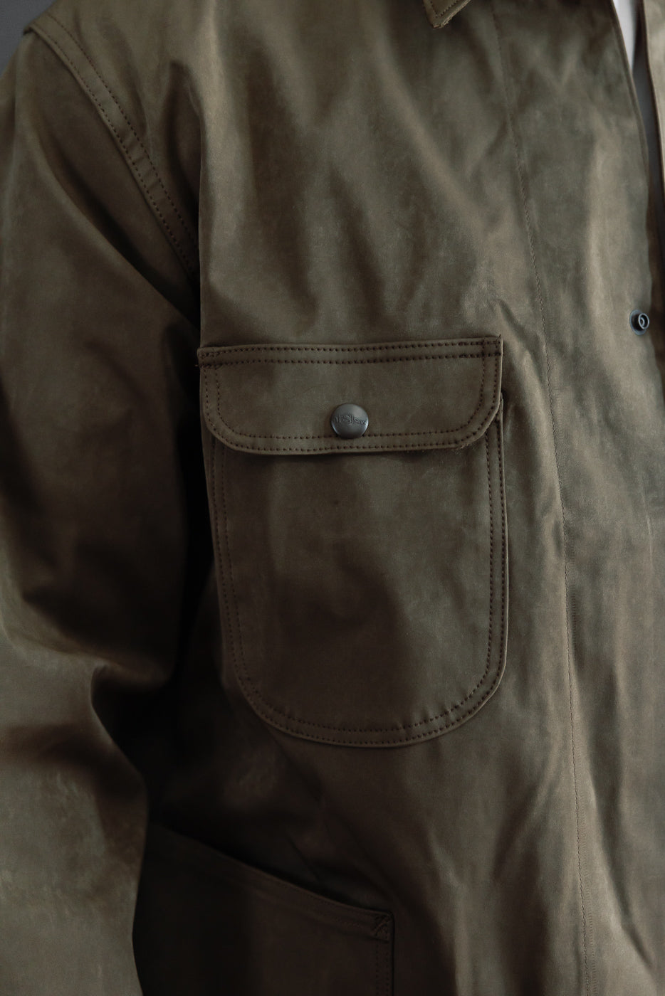 Close-up of the front left chest pocket on an olive brown waxed canvas jacket.