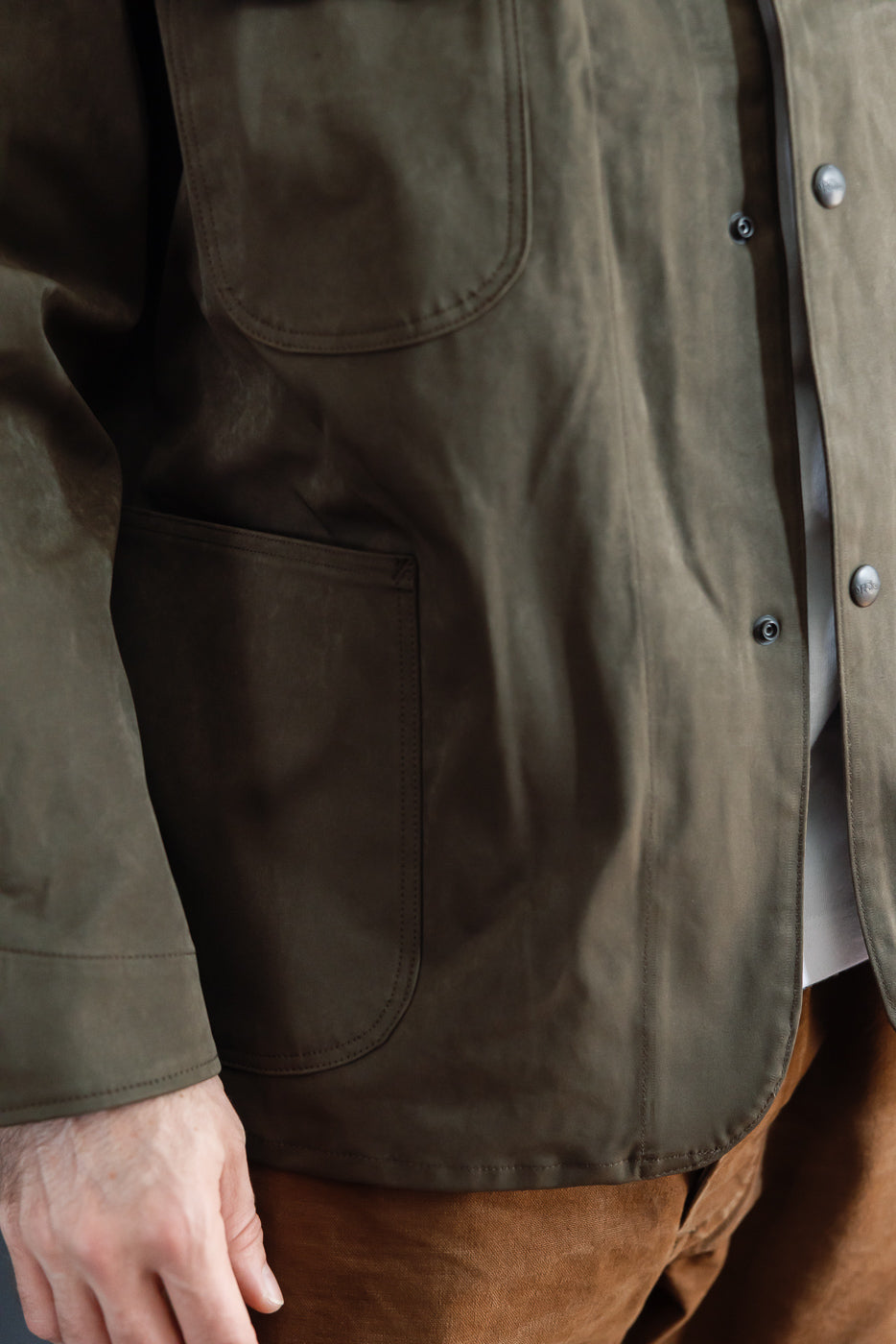 Close-up front view of a male model wearing an olive green canvas jacket with large patch pockets.