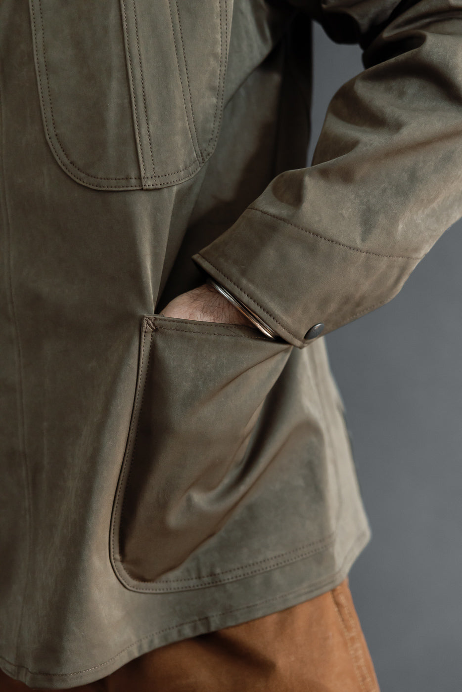 Close-up side view of a male model's hand in the pocket of a brown suede jacket.