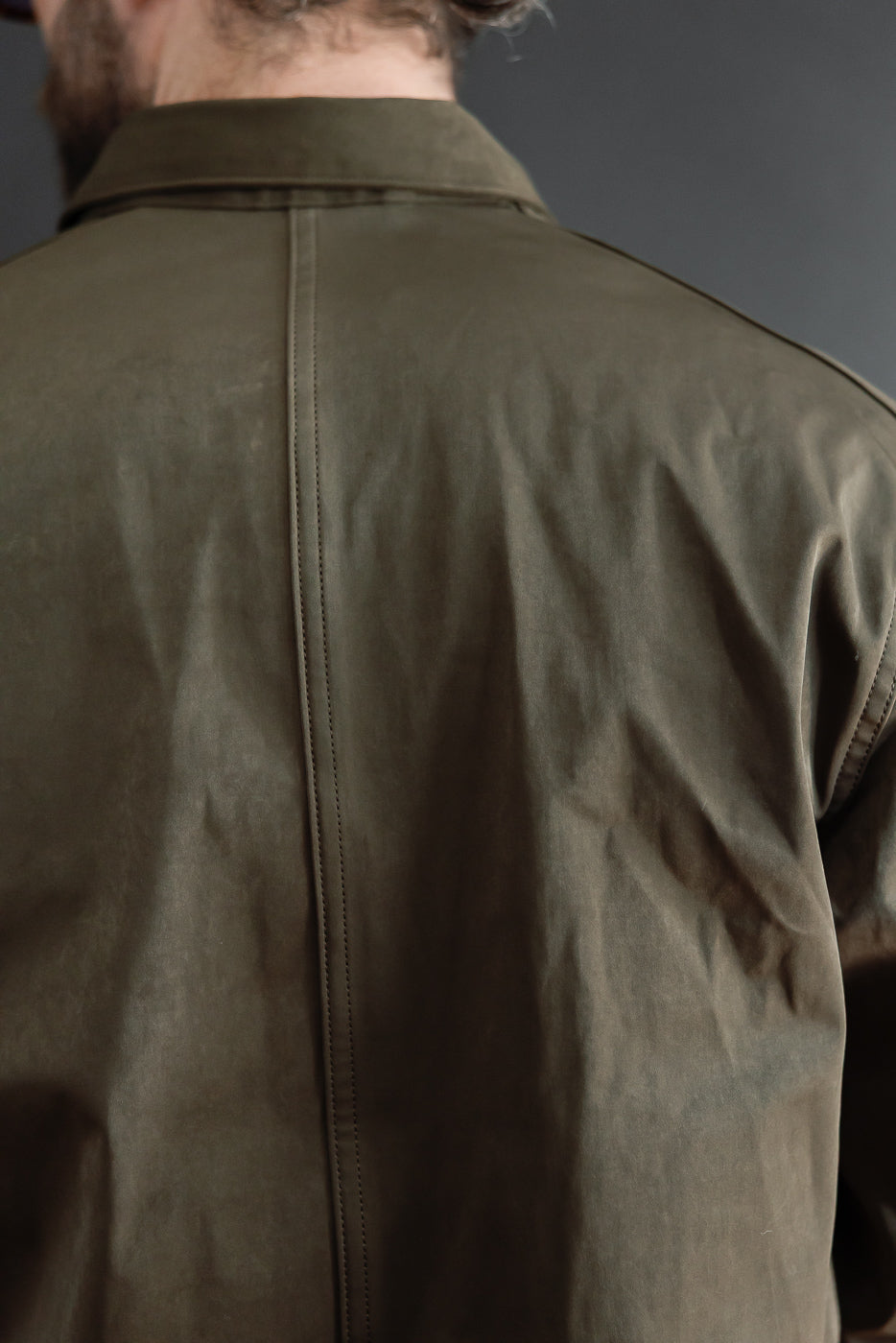 Close-up back view of an olive green jacket showing fabric texture and center seam detail.