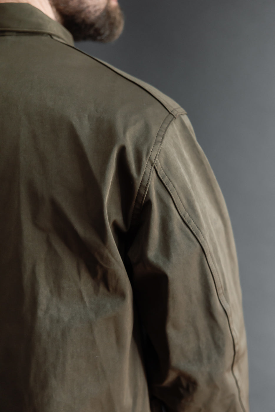 Close-up back view of an olive waxed jacket on a male model, 5'9