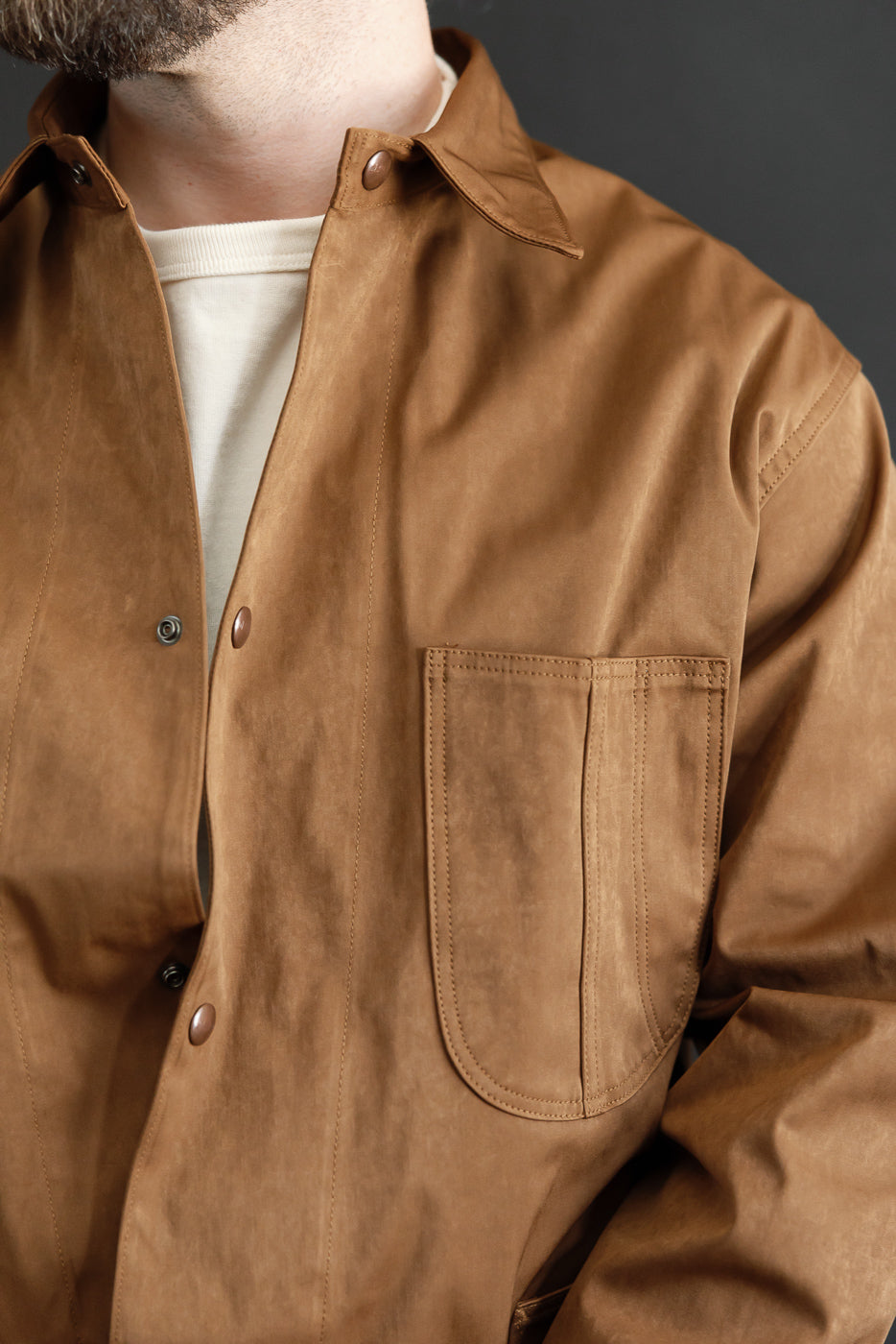 Close-up of front left chest pocket and collar of a brown jacket on a male model, 5'9