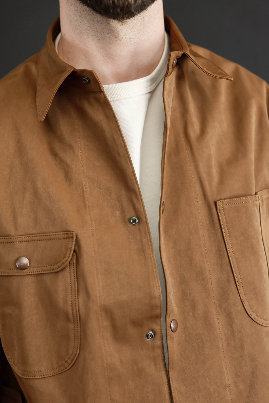 Close-up front view of a brown canvas button-down shirt showing collar and chest pocket detail.
