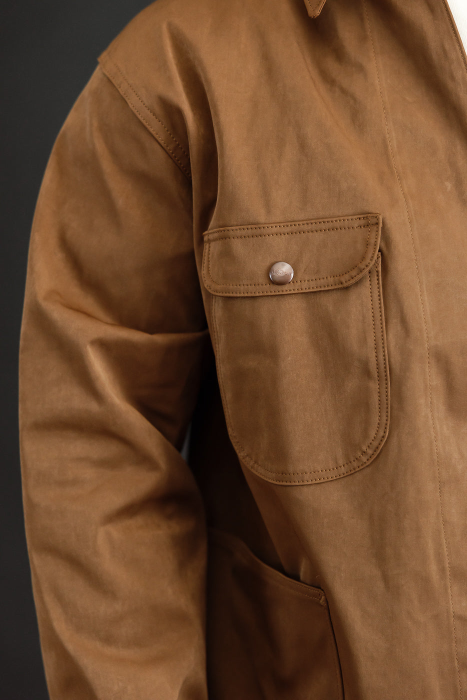 Close-up of the front chest pocket on a brown canvas work jacket showing button detail.