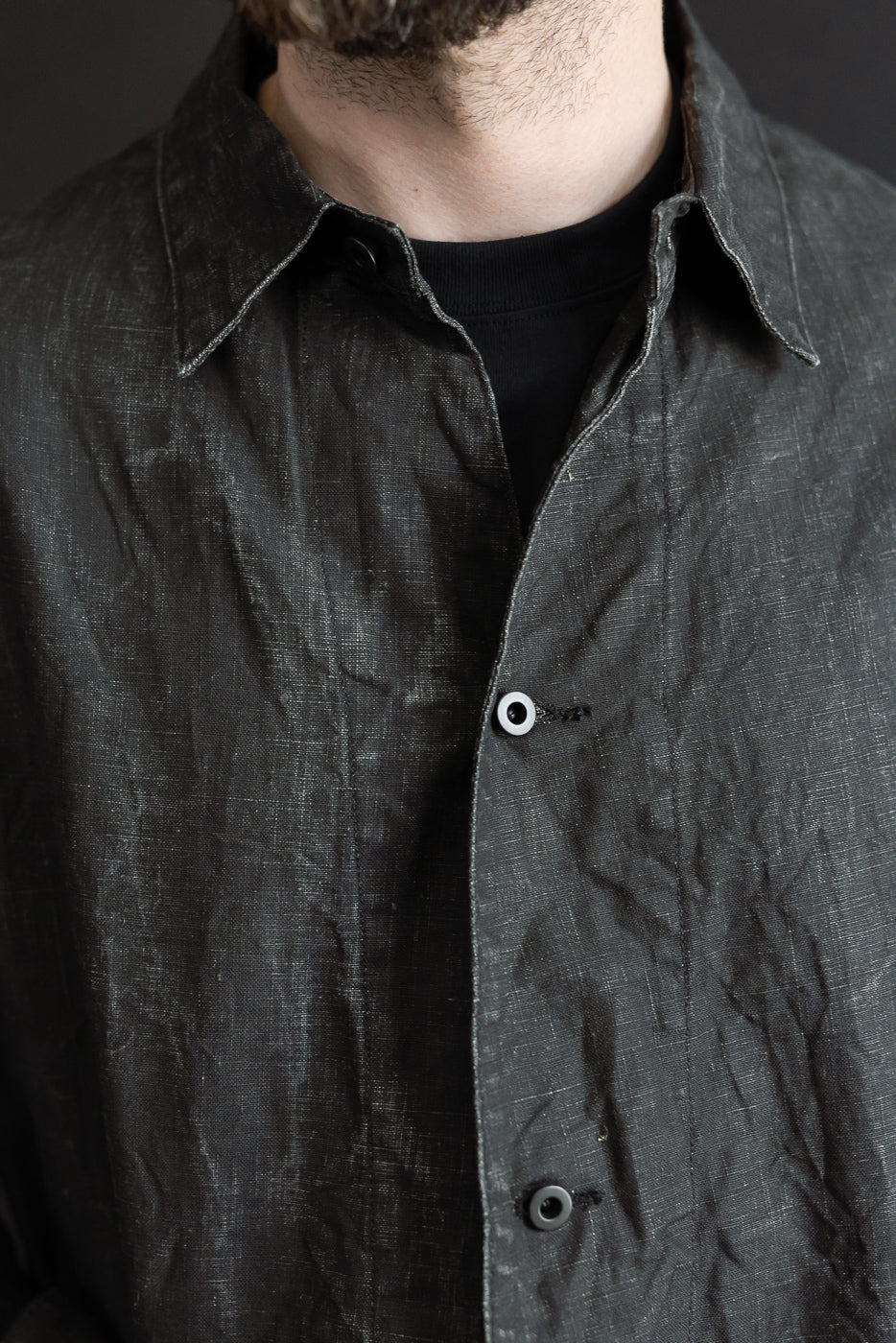 Close-up front of black linen coverall on male model, showing fabric texture and collar detail.