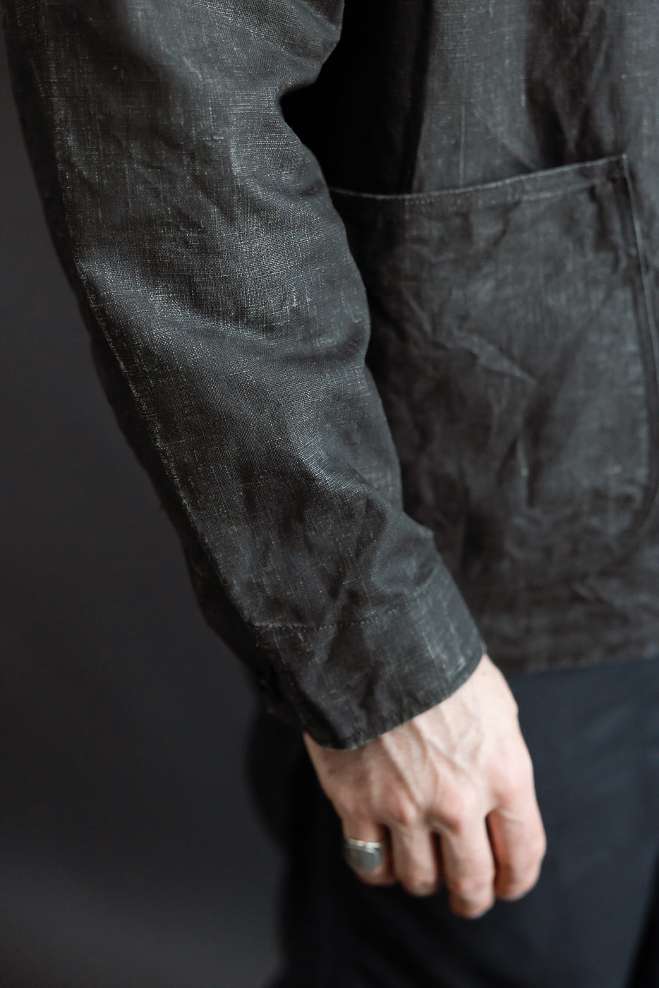 Close-up of male model's right arm and pocket, showing front side and sleeve texture of black linen coverall, model is 5'9