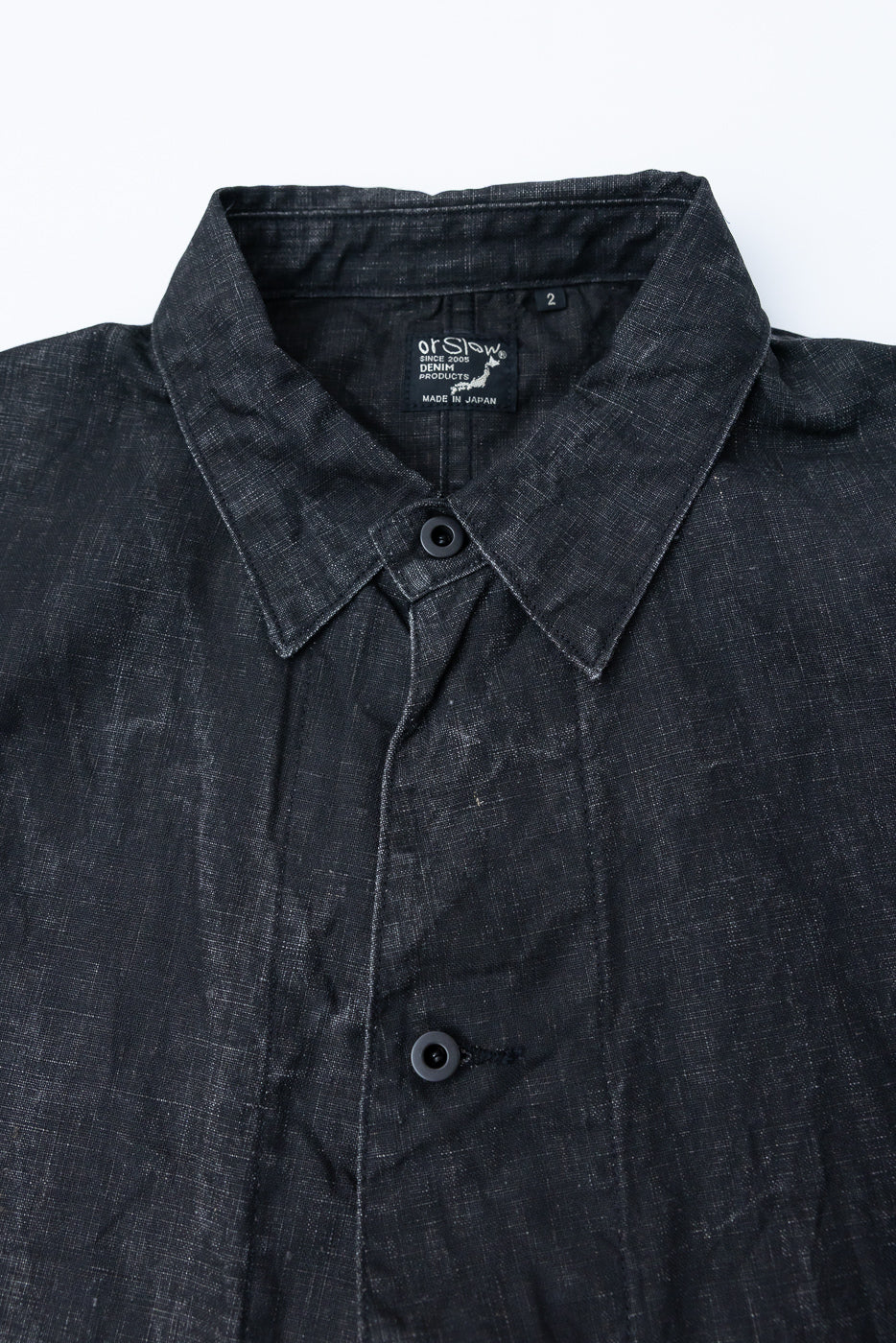 Close-up front view of black sumi-coated linen coverall, showing collar, buttons, fabric texture, and inner neck tag detail.