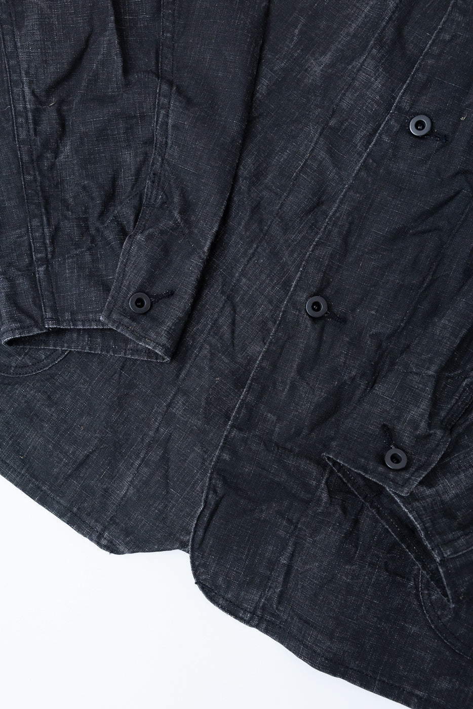 Close-up of black sumi-coated linen coverall front, showing button details and pocket stitching.