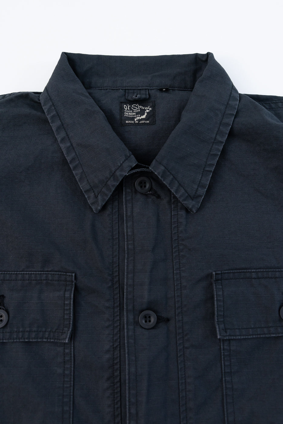 Close-up front view of dark denim shirt with collar, buttons, and tag detail, made in Japan.