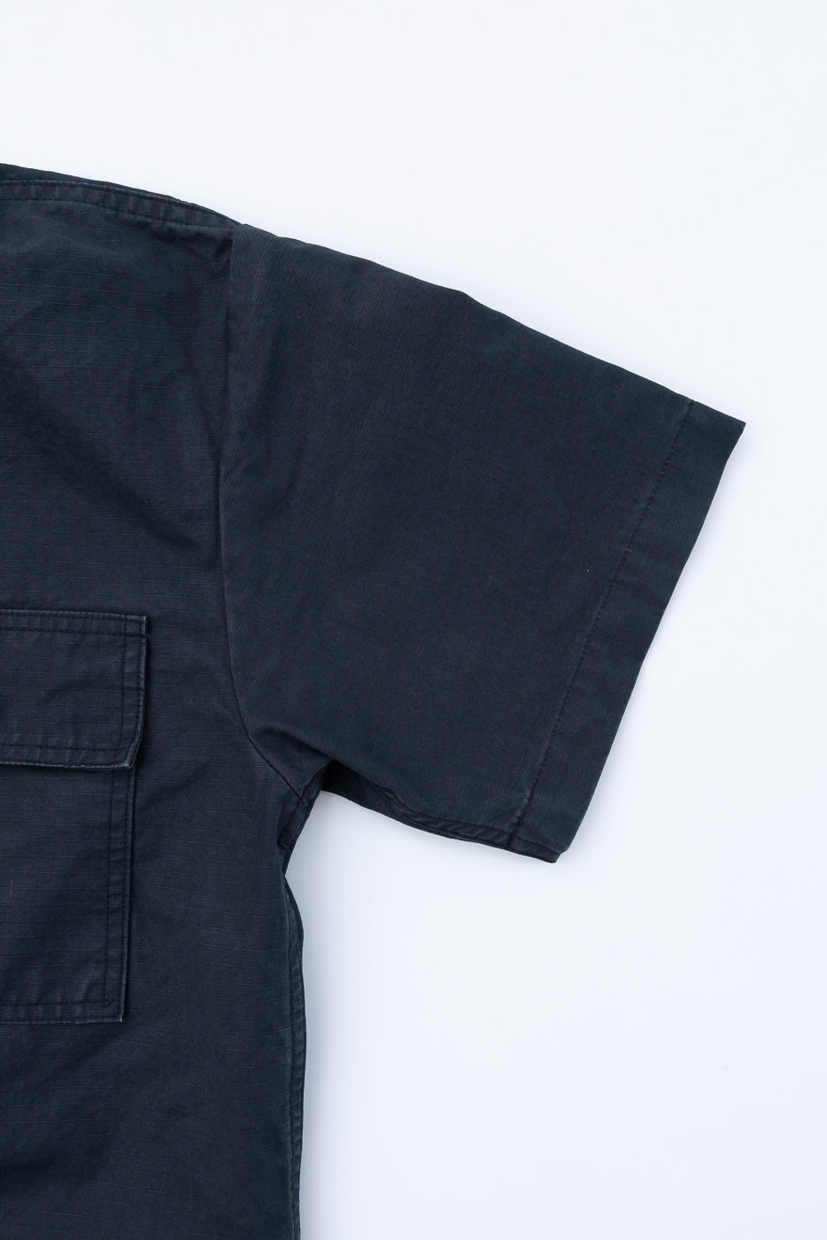 Close-up of black short-sleeve shirt front, showing chest pocket and sleeve hem detail