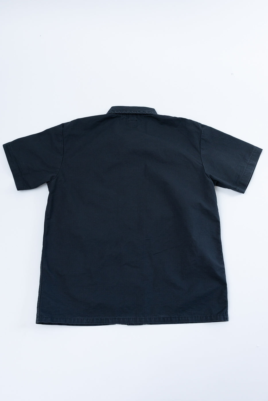 Back view flat lay of black short-sleeve shirt, showing collar, hem, and clean construction details.