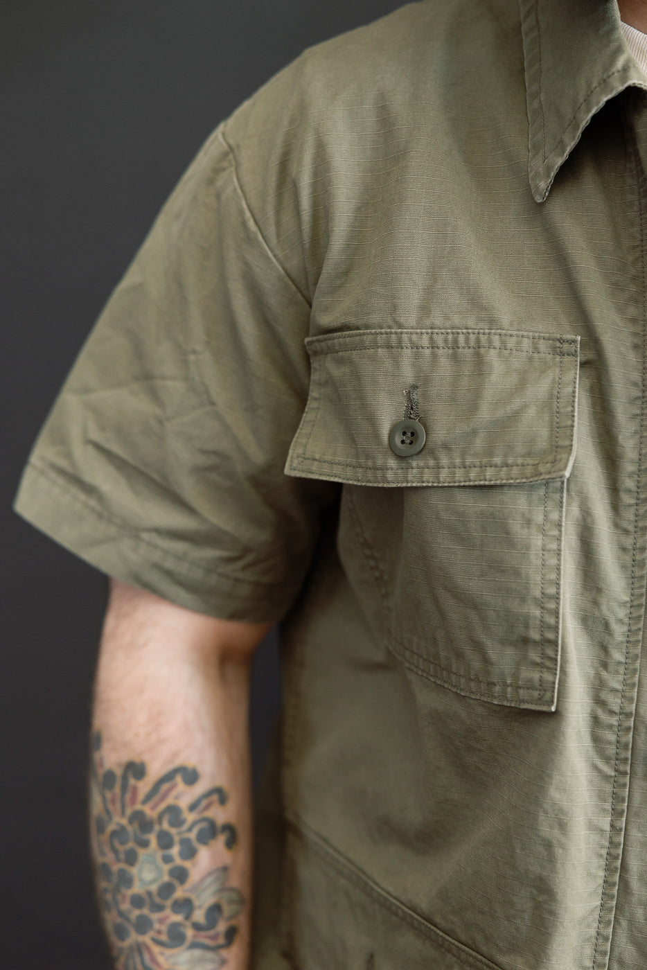 A close-up of a person wearing the orSlow 01-8046-76k Utility Short Sleeve Work Shirt Jacket in Army Green, showcasing the relaxed fit, button-flap chest pocket, and durable cotton fabric.