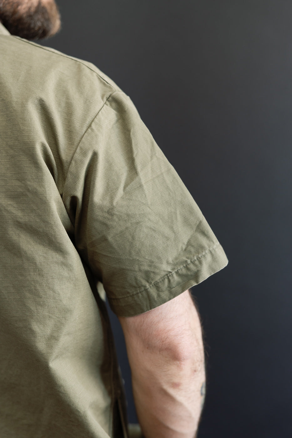Close-up of a person wearing the orSlow 01-8046-76k Utility Short Sleeve Work Shirt Jacket in Army Green, showcasing its durable ripstop fabric and relaxed fit, reflecting Dant's premium workwear aesthetic.