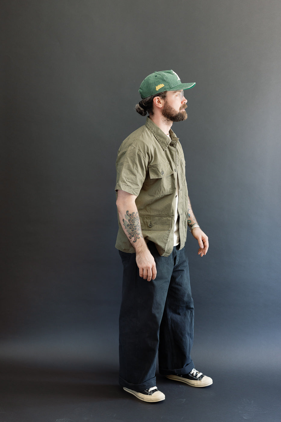 A man models the orSlow 01-8046-76k Utility Short Sleeve Work Shirt Jacket in Army Green, featuring a relaxed fit with chest utility pockets and short sleeves, embodying Dant's premium menswear aesthetic.