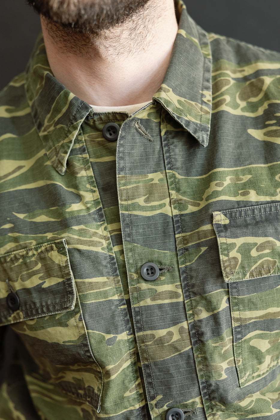 Close-up of an upper torso wearing the 01-8046 -TGC - Utility Short Sleeve Work Shirt Jacket in tiger camo, showcasing its relaxed fit, button-up style, and utility pockets.