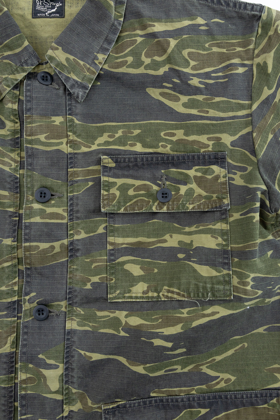 Close-up of the 01-8046 -TGC - Utility Short Sleeve Work Shirt Jacket - Tiger Camo, showcasing its green-and-brown camouflage pattern, button-flap pocket, and orSlow – Made in Japan label on the collar.