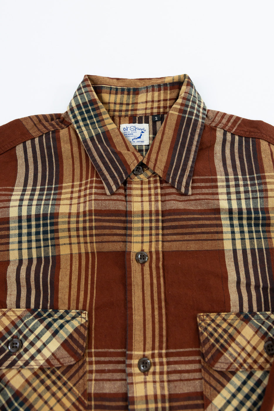 Close-up front view of men's plaid shirt with button-down collar, chest pockets, and 'ot Slow' tag, showcasing fabric texture and pattern details.