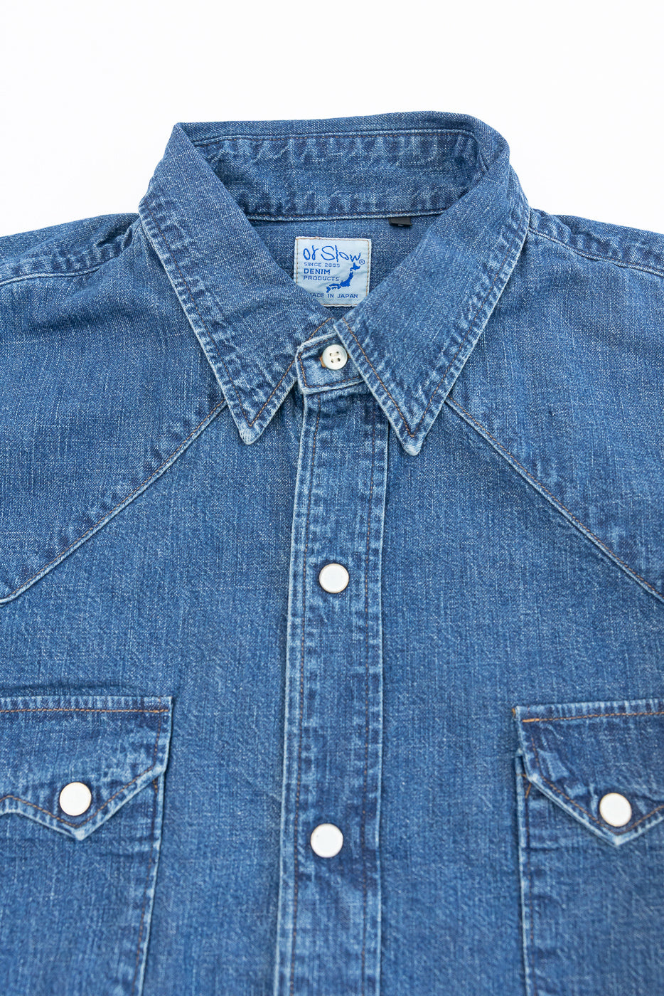 Close-up of the front collar and upper chest of a blue denim shirt showing a brand tag.