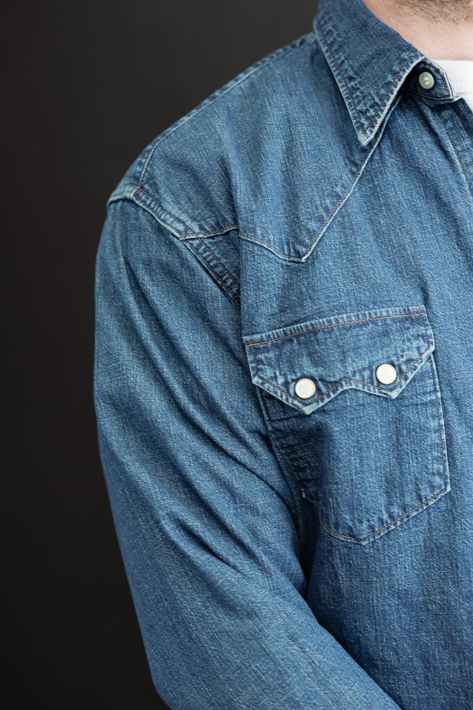 Close-up of the left chest and shoulder of a blue denim shirt showing the western yoke and pocket.