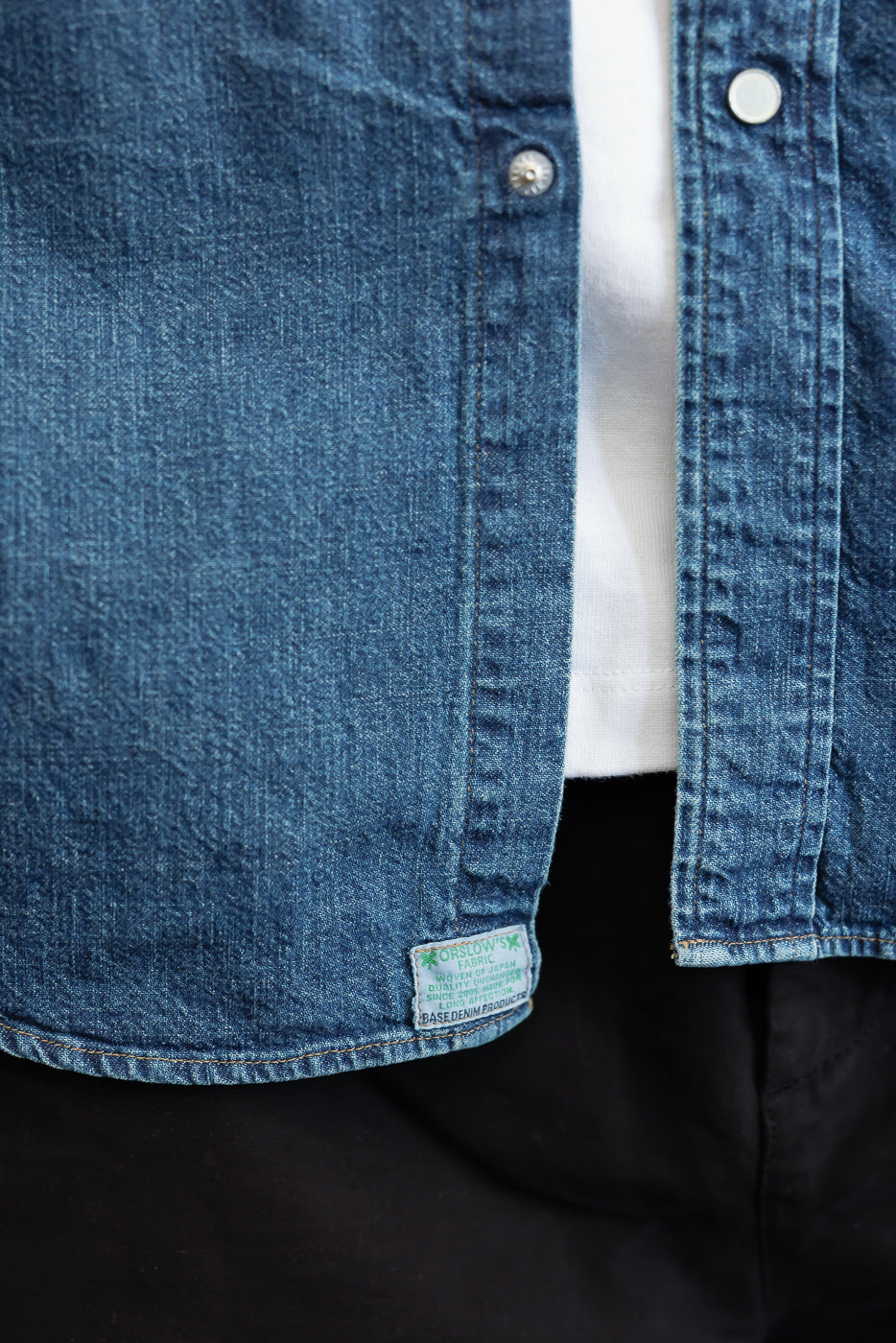 Close-up front view of blue denim shirt fabric texture and bottom hem detail.