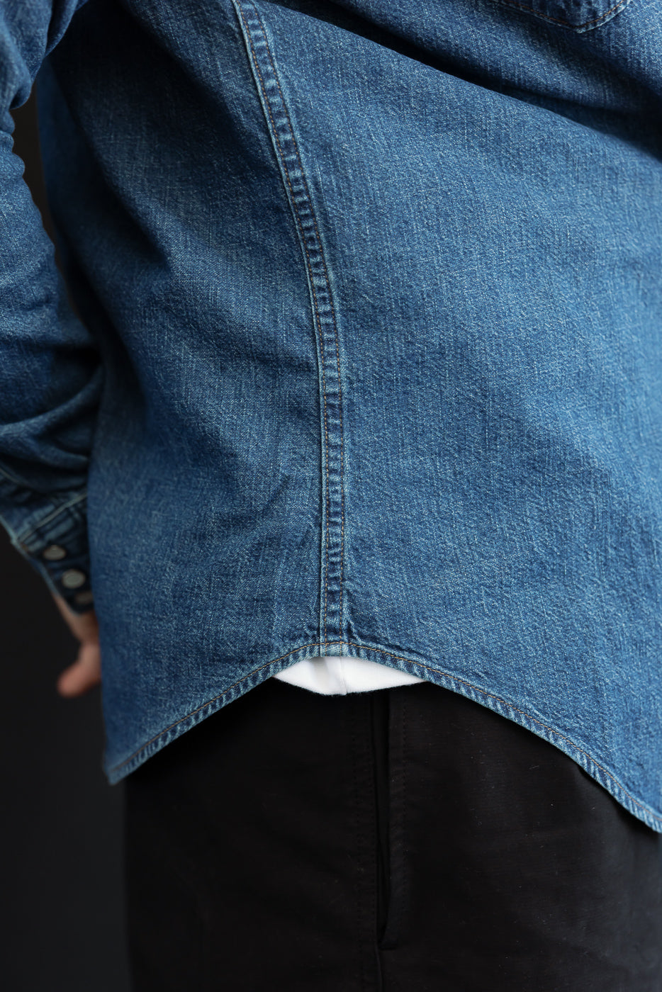 Close-up back view of a male model wearing a blue denim shirt, showing the hem and vertical seam.