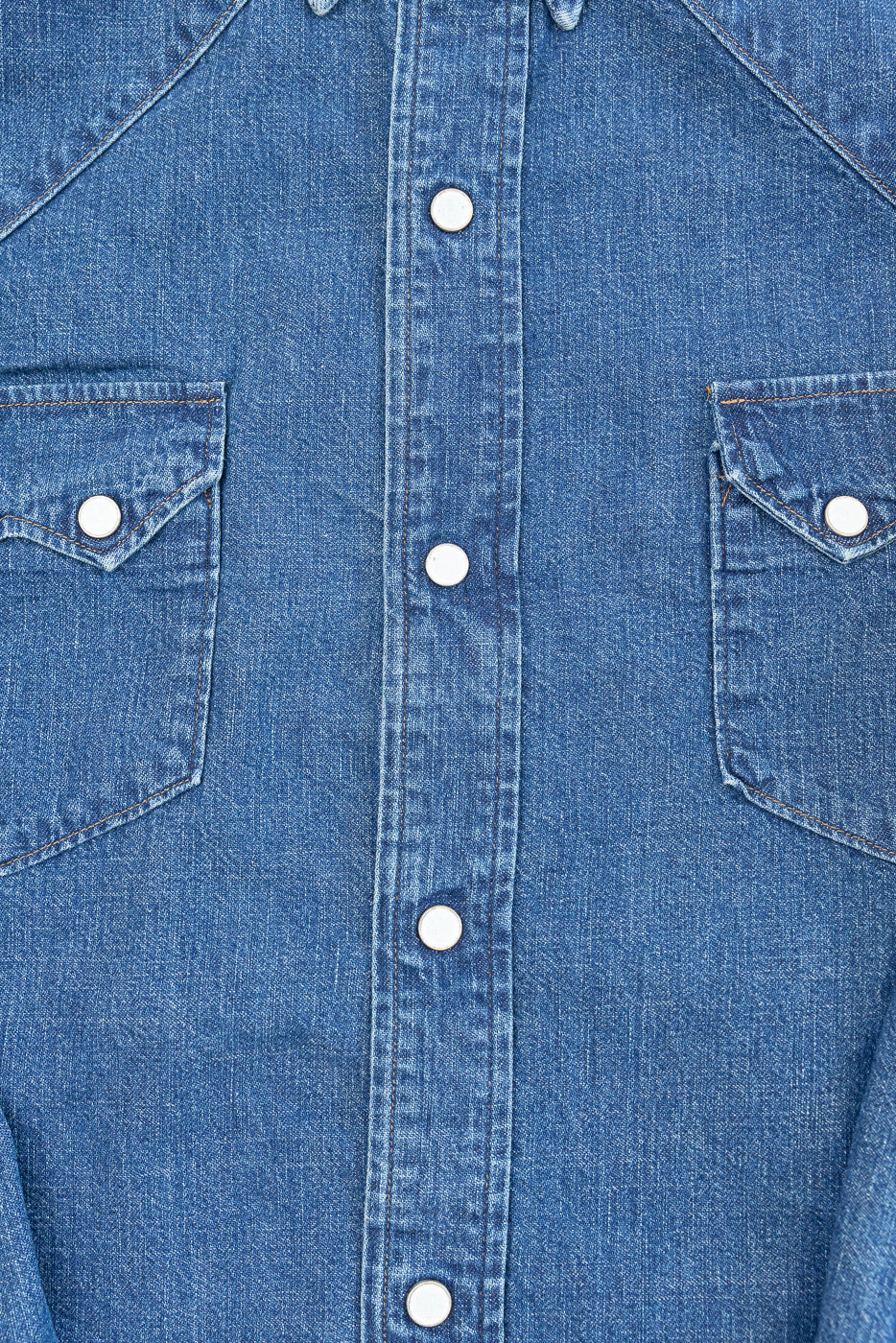 Close-up of the front of a blue denim shirt showing buttons and chest pockets.