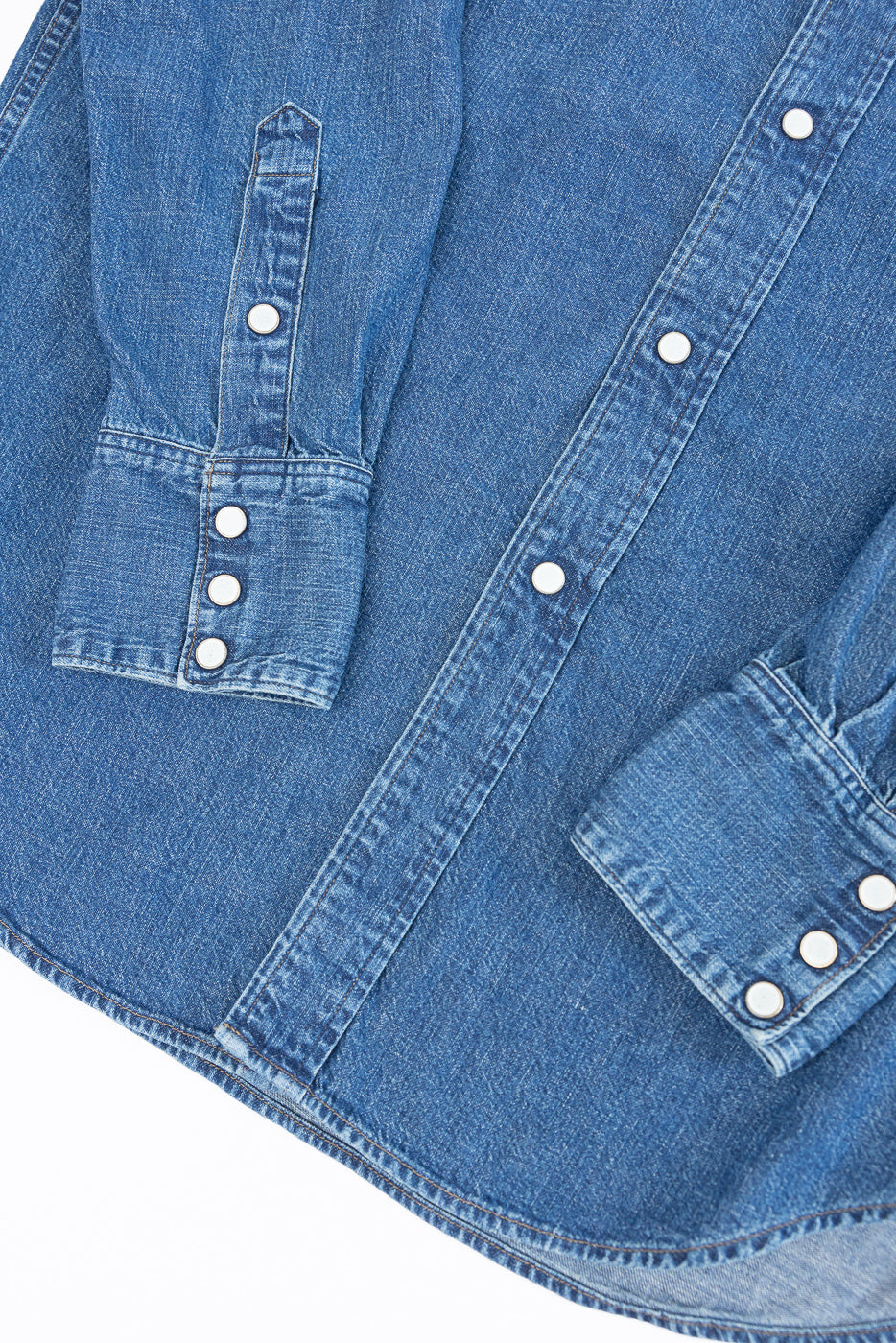 Close-up of the front of a blue denim shirt showing the buttoned placket and sleeve cuffs.