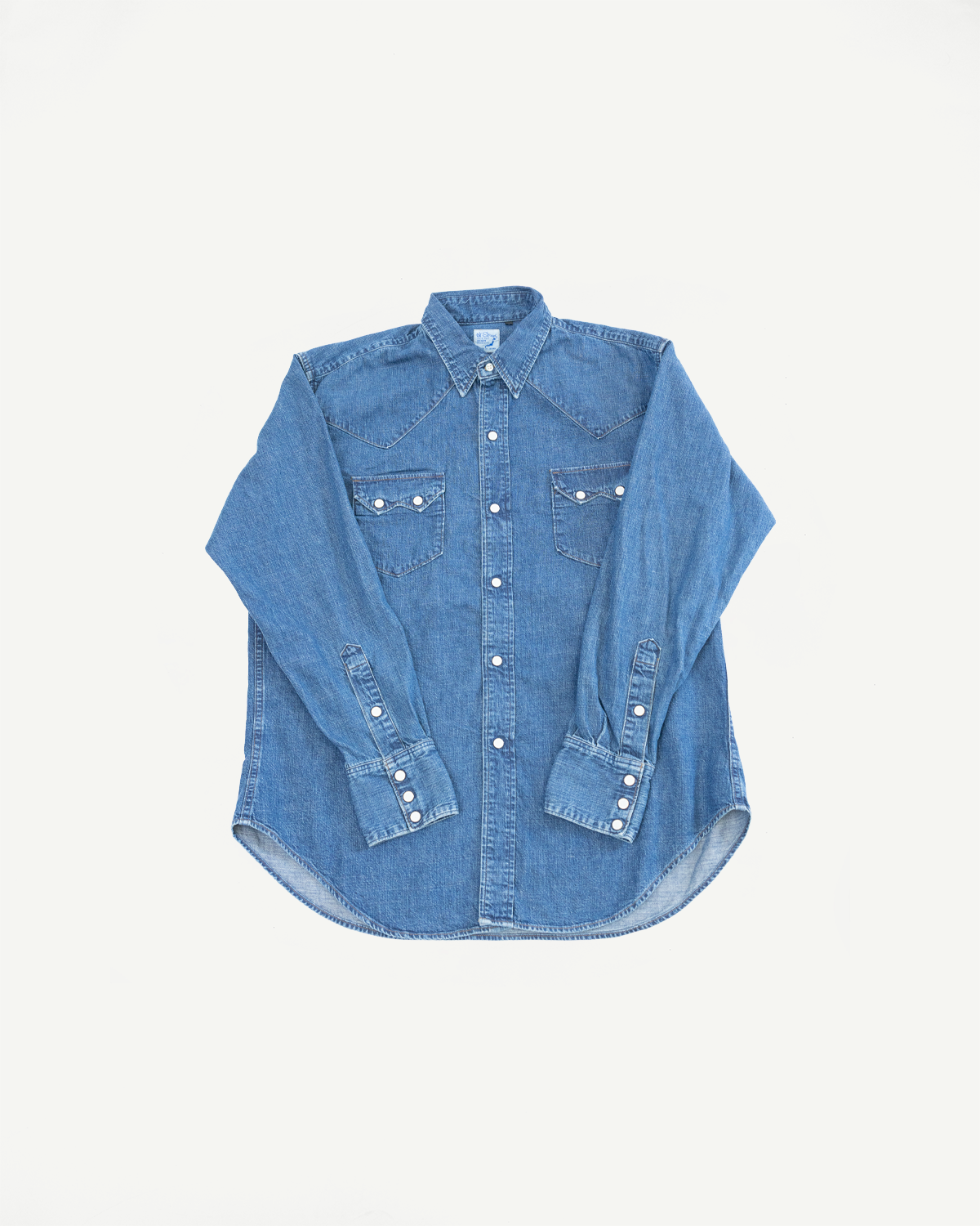 Front view flat lay of a long-sleeve blue denim button-down shirt with chest pockets and pearl snaps.
