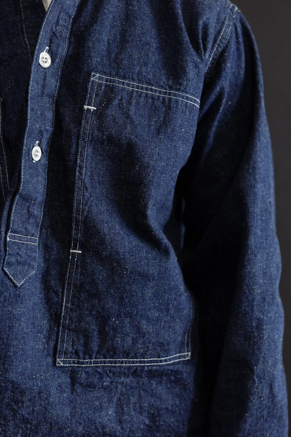 Close-up of the front left chest pocket and button placket on a dark indigo denim shirt.