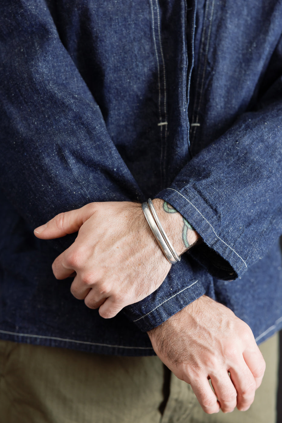 Close-up front view of a male model's wrists wearing silver bangles and a denim shirt.