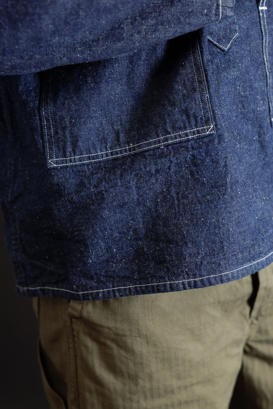 Close-up of the front side of a male model's dark indigo denim jacket, showing the pocket and texture.
