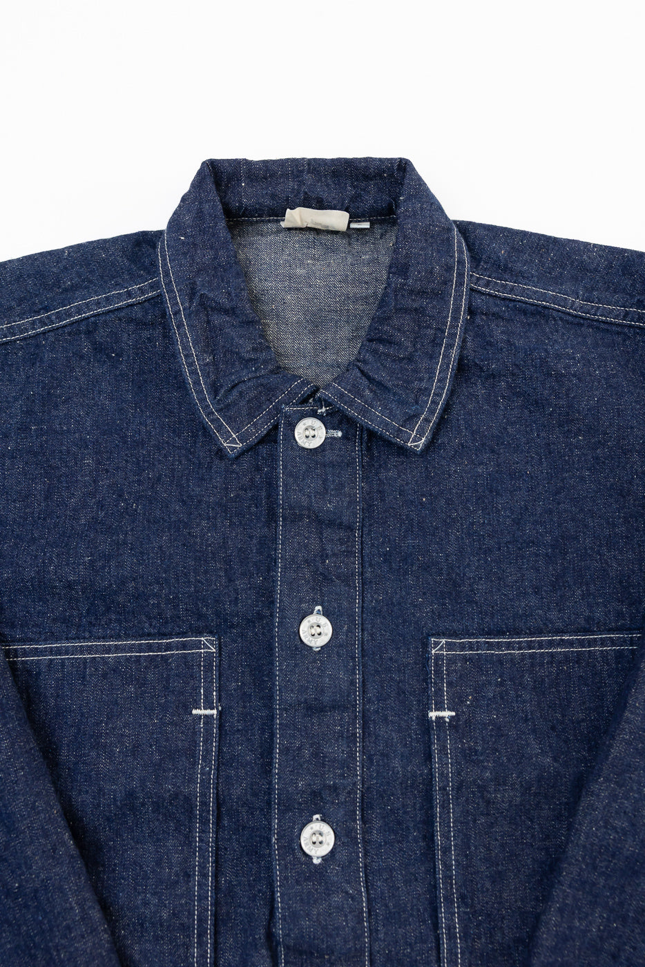 Close-up front view of a dark blue selvedge denim shirt showing the collar, buttons, and chest pockets.