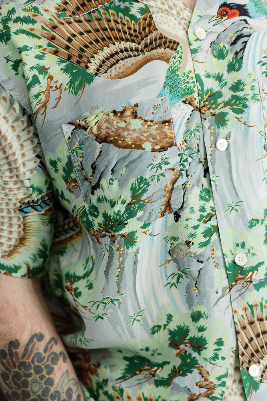 Close-up front view of men's short-sleeve shirt with bird & forest print, white buttons, chest pocket; model 5'9