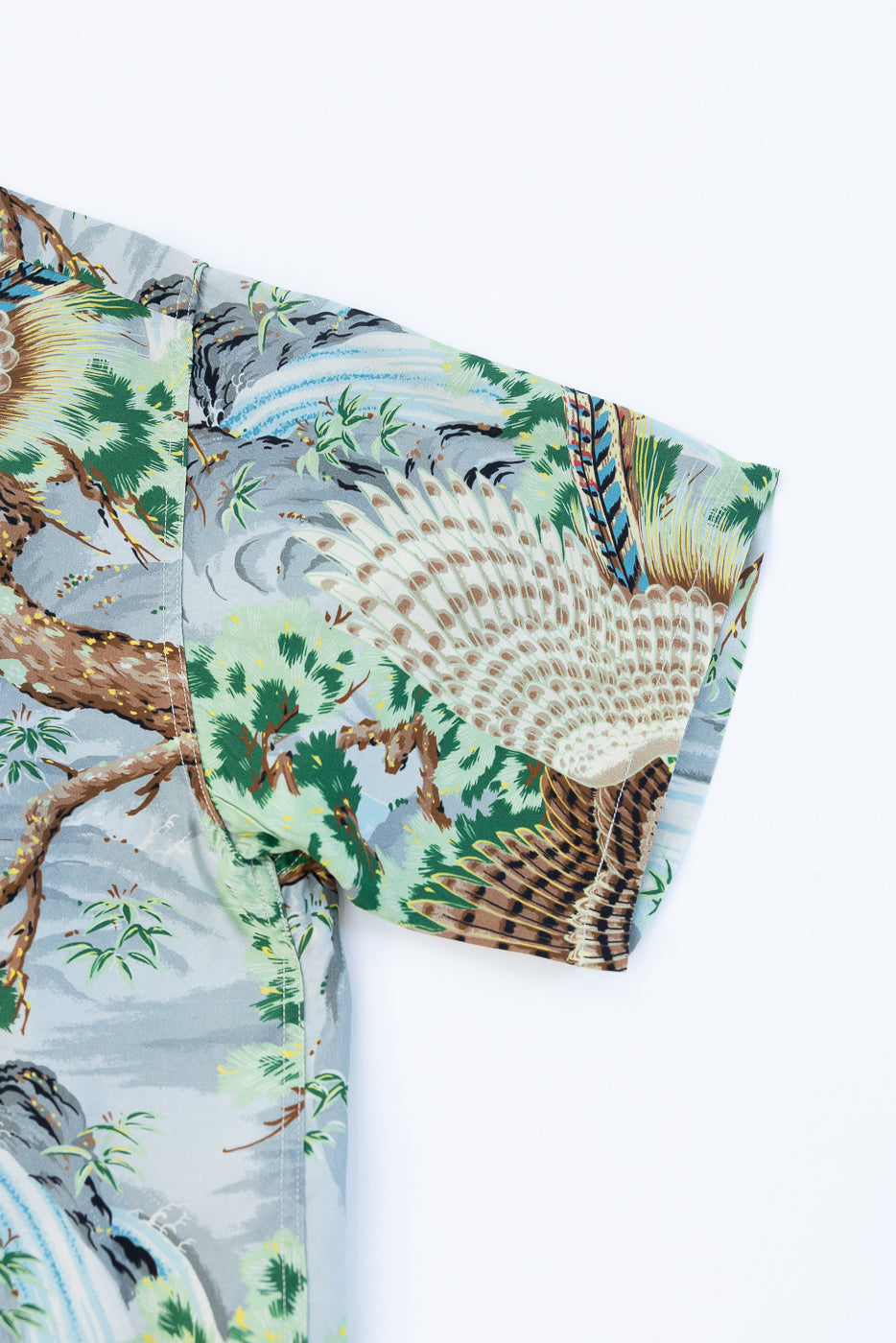 Close-up of men's short-sleeve shirt front, showcasing peacock and nature print, fabric texture, and sleeve detail.