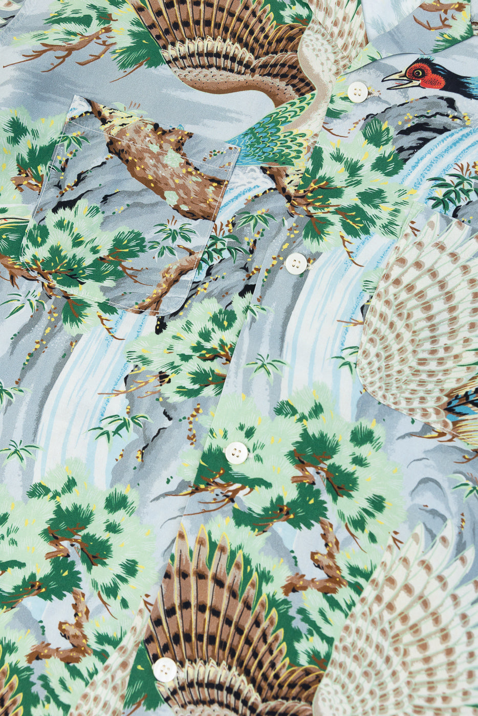 Close-up front view of men's button-up shirt with bird, tree, waterfall print, white buttons, chest pocket