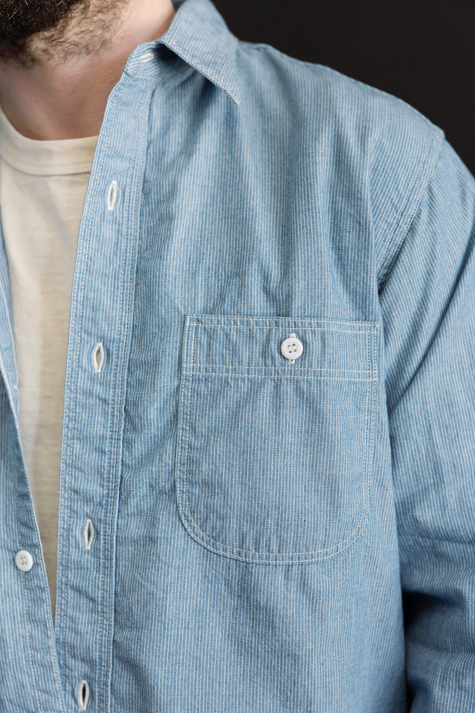 Close-up of the upper torso wearing the orSlow 01-8270-181k - Relaxed Fit Chambray Work Shirt - Hickory, showcasing its hickory stripe pattern, button-down front, and single chest pocket over a T-shirt.