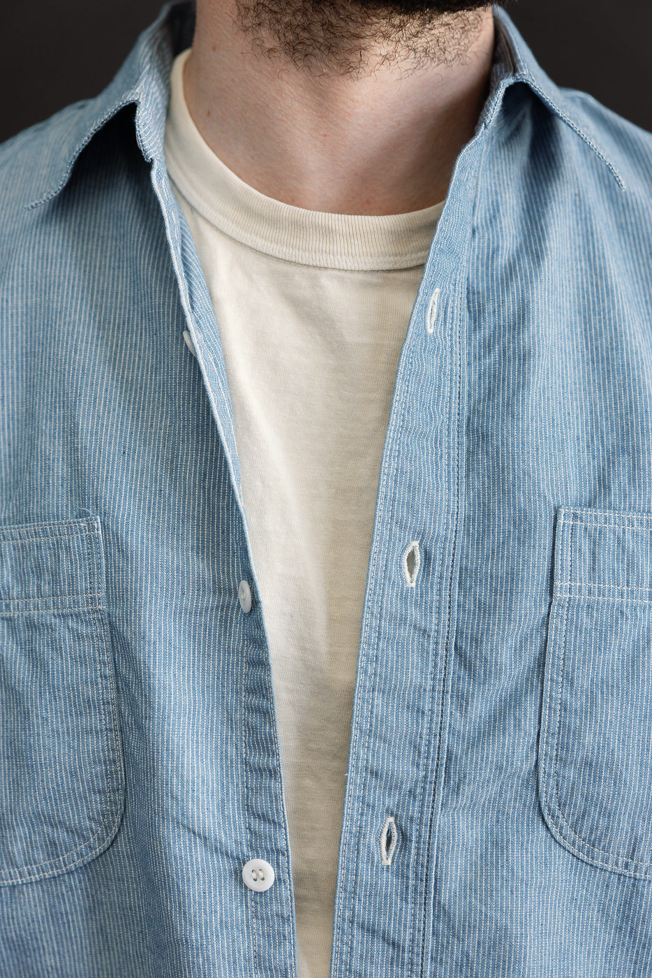 Close-up of the 01-8270-181k Relaxed Fit Chambray Work Shirt - Hickory, showcasing its light-blue, thinly striped pattern over a plain white T-shirt, highlighting its casual, vintage-inspired design.