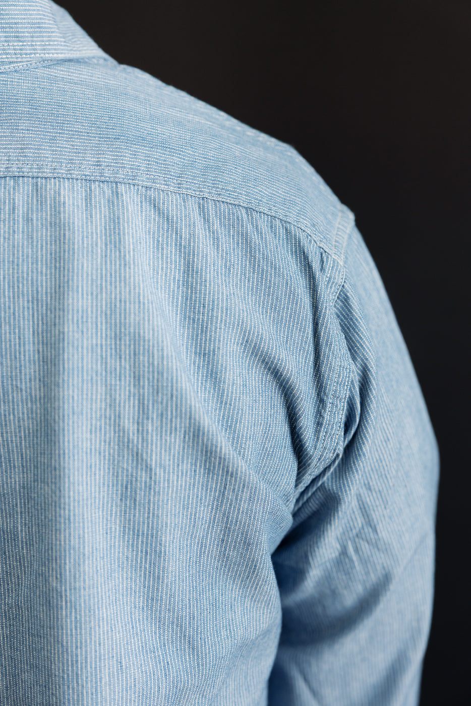 Close-up of the upper back of the 01-8270-181k Relaxed Fit Chambray Work Shirt - Hickory, showcasing its light blue fabric with subtle white vertical stripes, reflecting American workwear and naval heritage.