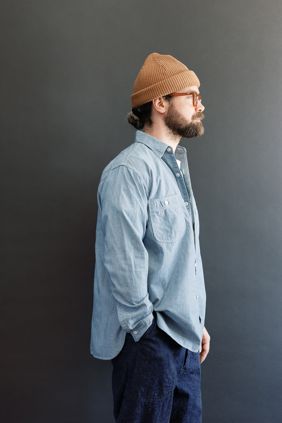 A bearded man models the 01-8270-181k Relaxed Fit Chambray Work Shirt - Hickory, featuring a hickory stripe pattern and dagger collar, exemplifying Dant's heritage-inspired workwear collection.