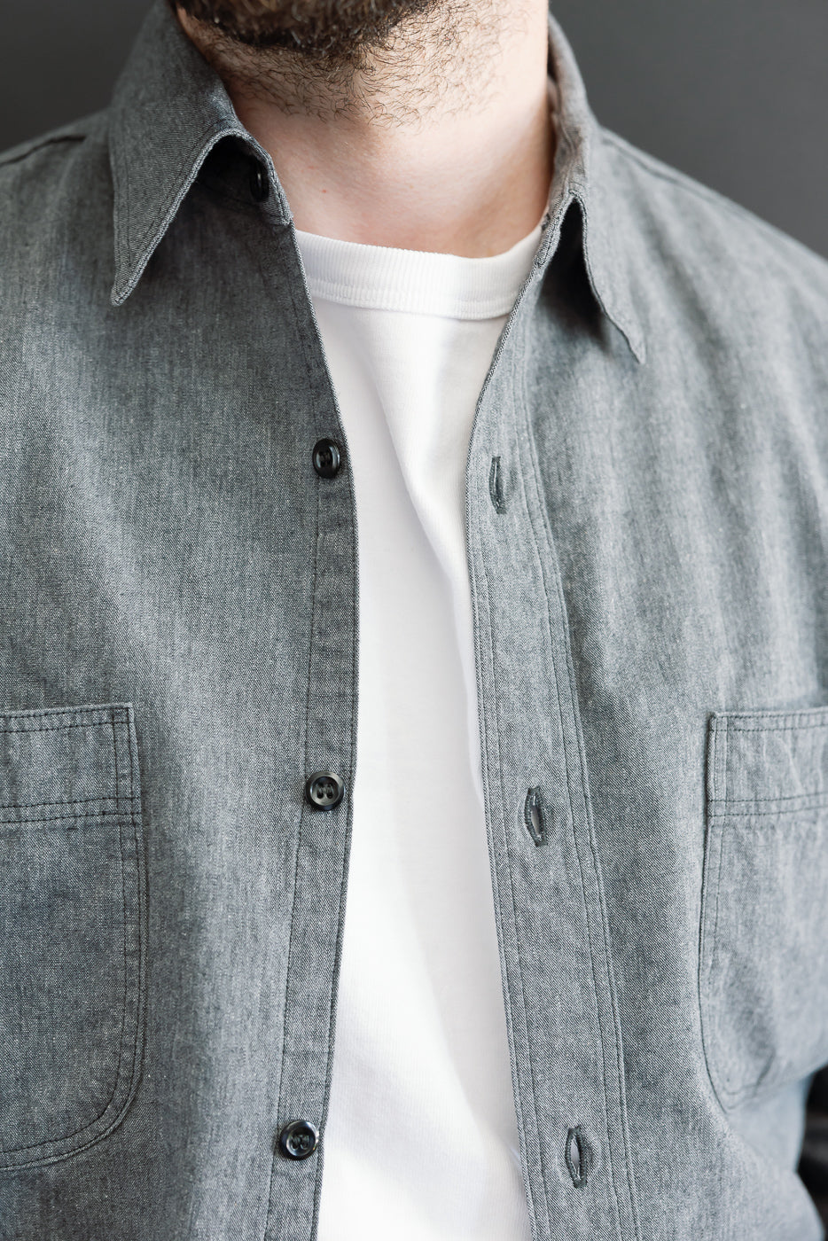 Close-up front view of a male model wearing a grey button-down shirt over a white t-shirt.