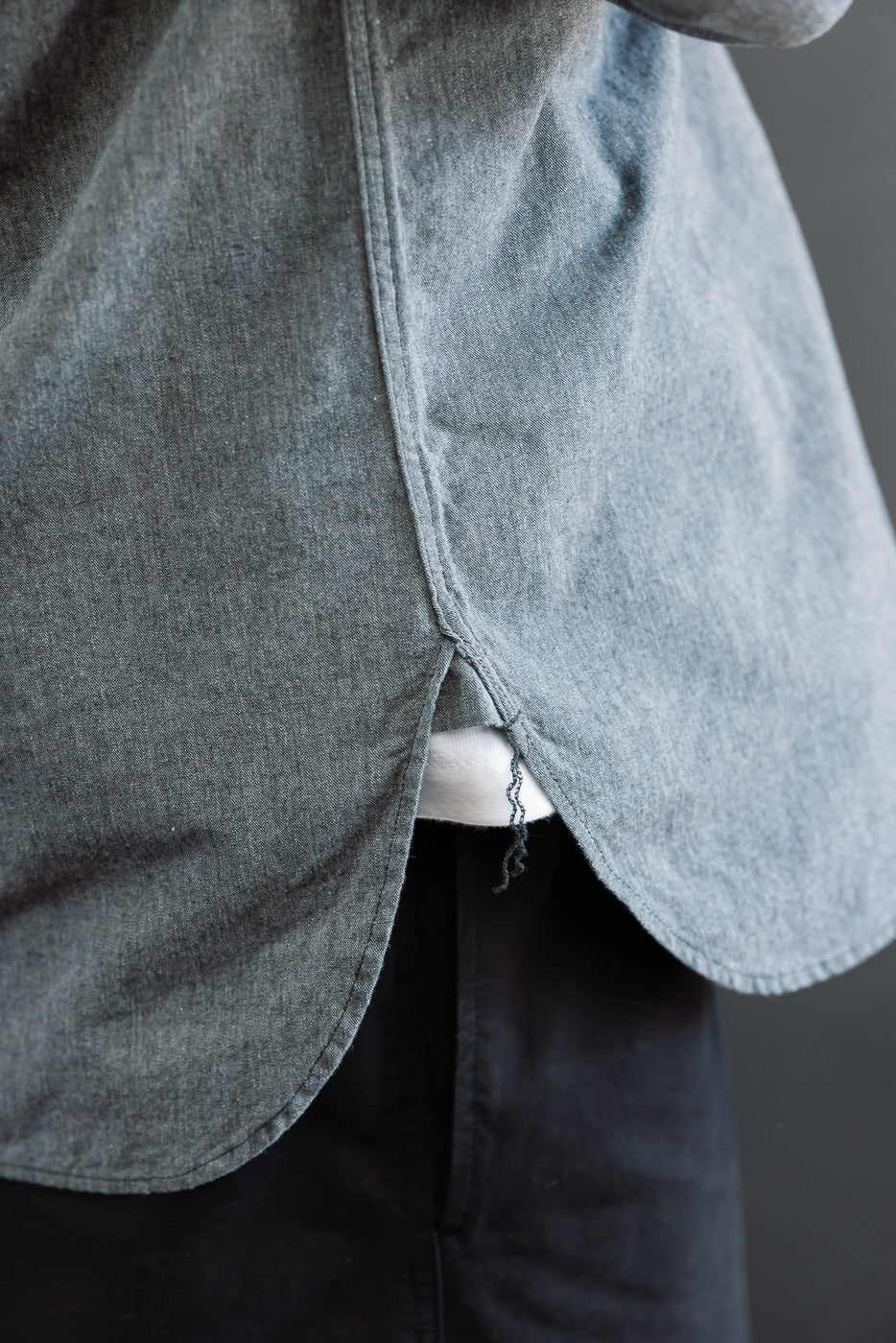 Close-up of the back hem of a grey shirt showing a center vent and white selvedge detail.