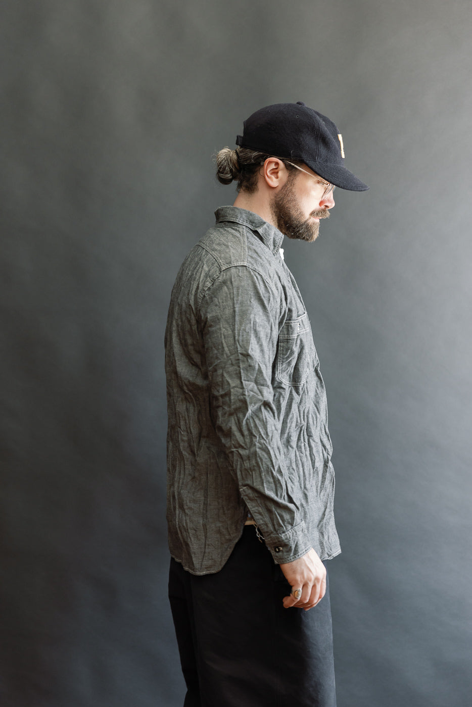 A bearded man in profile wears the orSlow 01-8270-61 Relaxed Fit Chambray Work Shirt. The shirt showcases a slightly crinkled texture, double chest pockets, and a relaxed, vintage-inspired silhouette.