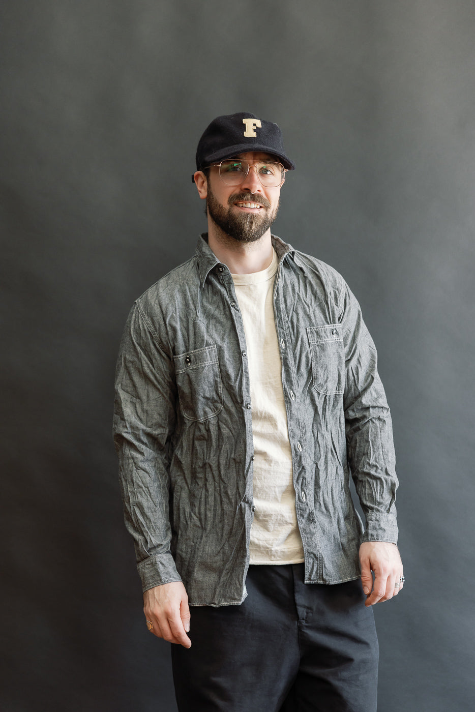 A man models the 01-8270-61 Relaxed Fit Chambray Work Shirt - Black, styled open over a T-shirt, highlighting its vintage-inspired, roomy silhouette and crinkled texture, embodying modern-casual workwear.
