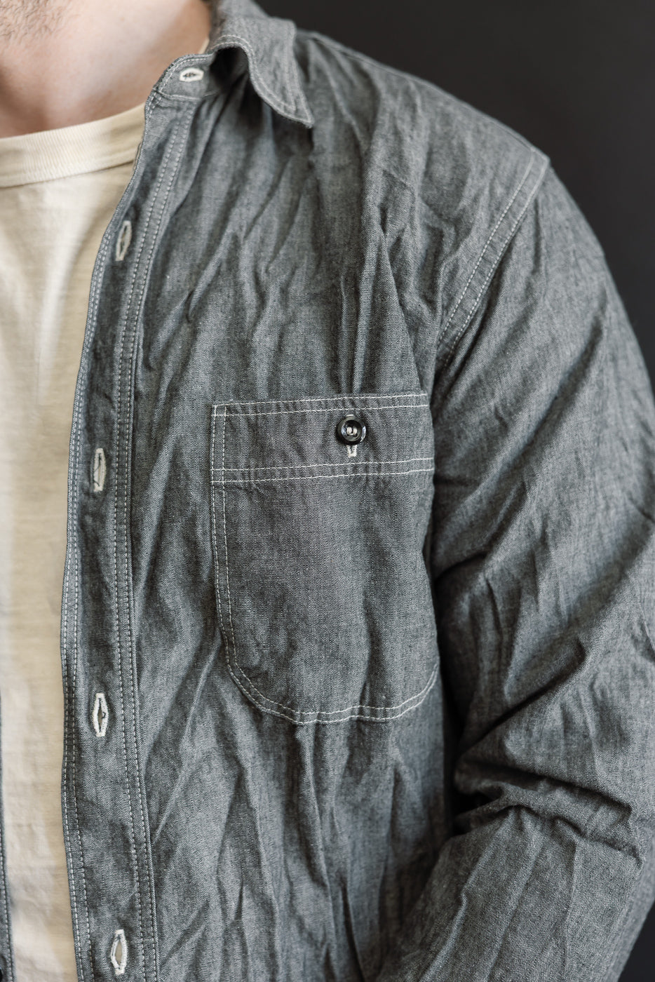 Person wearing orSlow’s 01-8270-61 Relaxed Fit Chambray Work Shirt in charcoal-gray, showcasing its classic 1940s workwear-inspired design with a single chest pocket and visible white top-stitching.