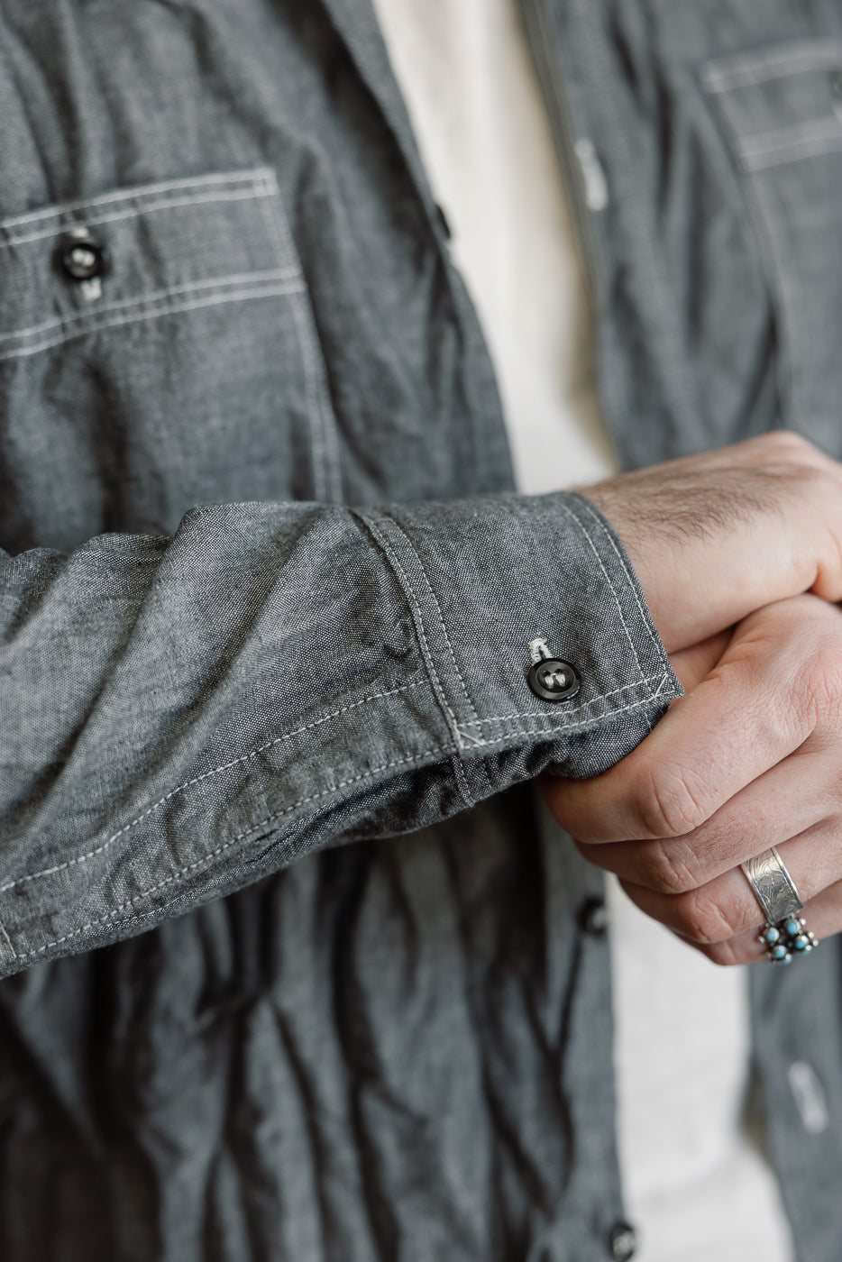 Close-up of a person adjusting the cuff of orSlow's 01-8270-61 Relaxed Fit Chambray Work Shirt, showcasing its button details, stitched pocket, and lightweight cotton chambray texture.