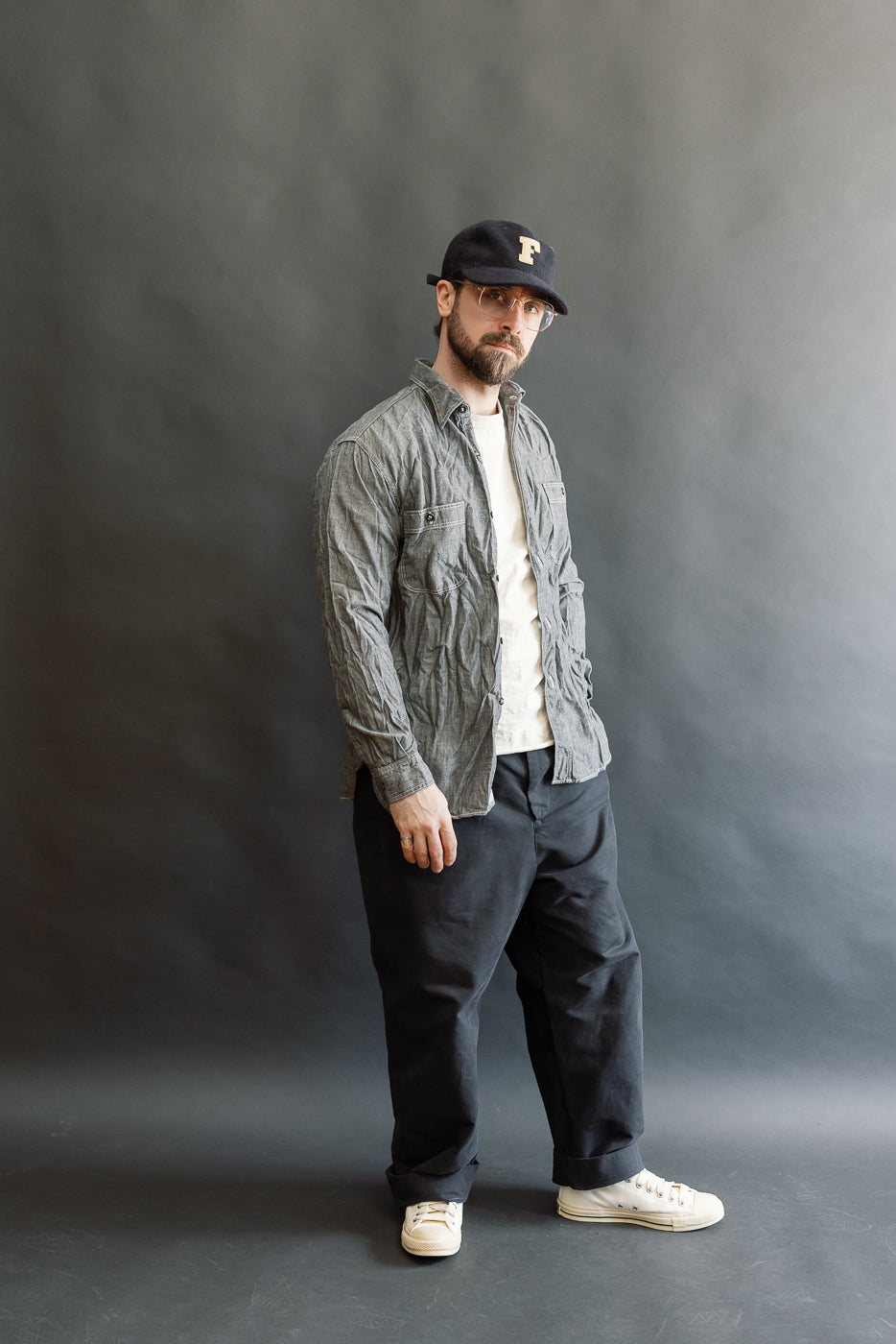 A man models the 01-8270-61 Relaxed Fit Chambray Work Shirt in black, styled over a T-shirt with loose-fit trousers and sneakers, embodying vintage 1940s workwear in a modern, relaxed silhouette.