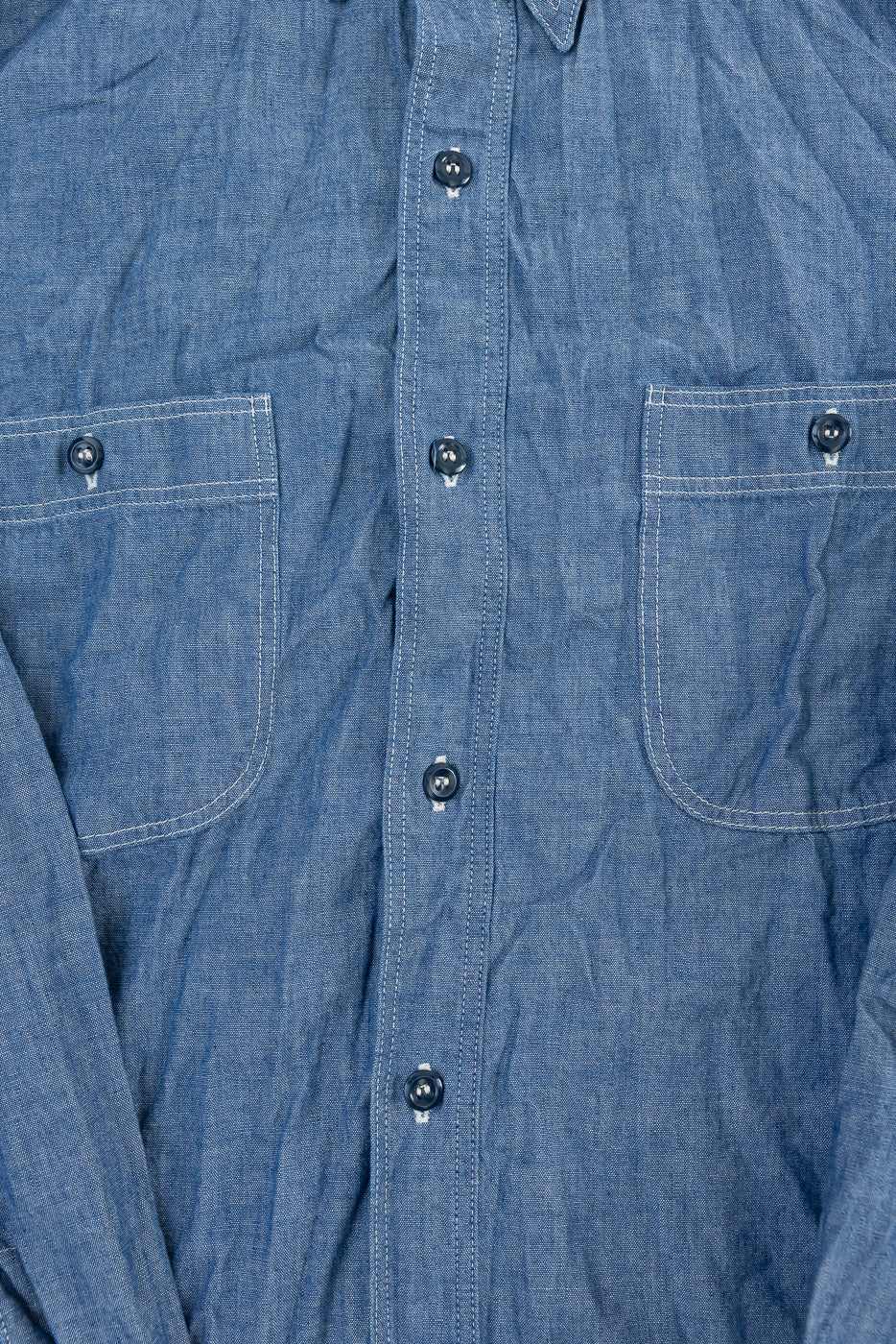 Close-up of front chest area of indigo chambray work shirt showing buttons, fabric texture, and dual button-flap pockets.